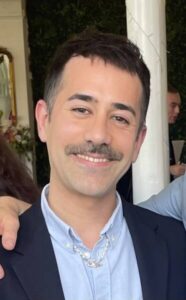 Photo of Diego Garcia. He has short dark hair, a moustache, he is in a light blue shirt and suit jjacket. He is smiling.